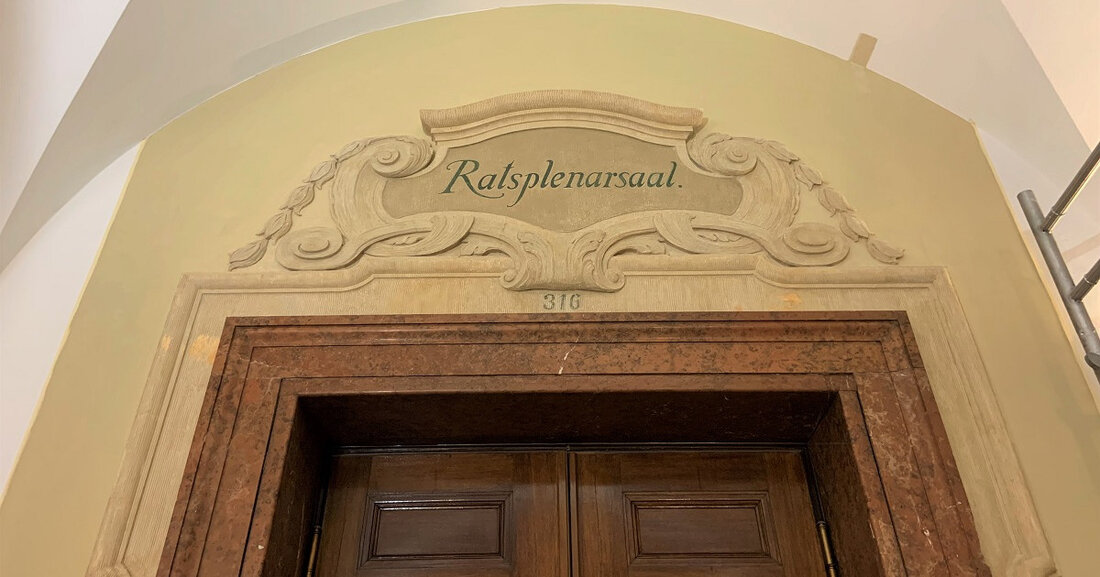 Historische Ornamente im Neuen Rathaus freigelegt Restauratoren haben am Ratsplenarsaal im Neuen Rathaus historische Ornamente und Farbschichten aus der Entstehungszeit des Gebäudes freigelegt. Die Arbeiten im Auftrag des Amtes für Gebäudemanagement haben rund neun Wochen gedauert und sind jetzt abgeschlossen: Millimeter für Millimeter wurden mit Skalpell unter bis zu acht Farbschichten die originale Wandfarbe sowie Schmuckornamente hervorgeholt – etwa der dunkelgrüne Schriftzug „Ratsplenarsaal“ sowie die frühere Zimmernummer 316 über dem Türsturz. Unter mehreren Farbschichten verbargen sich Ornamente und der Original-Schriftzug des Ratsplenarsaals aus der Entstehungszeit des Gebäudes. Freigelegt wurden insgesamt etwa fünf Quadratmeter zwischen Wandsockel und Decke, die jetzt als &hellip;